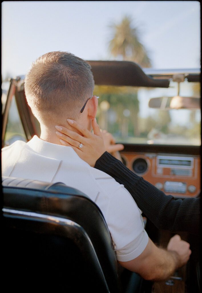 woman's hand on the back of man's neck as he drives a convertible