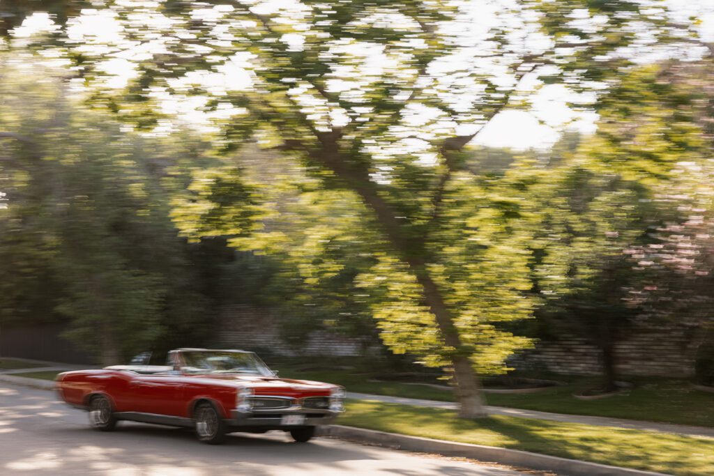 Blurred Red 1967 Pontiac GTO driving down tree lined street in Los Angeles