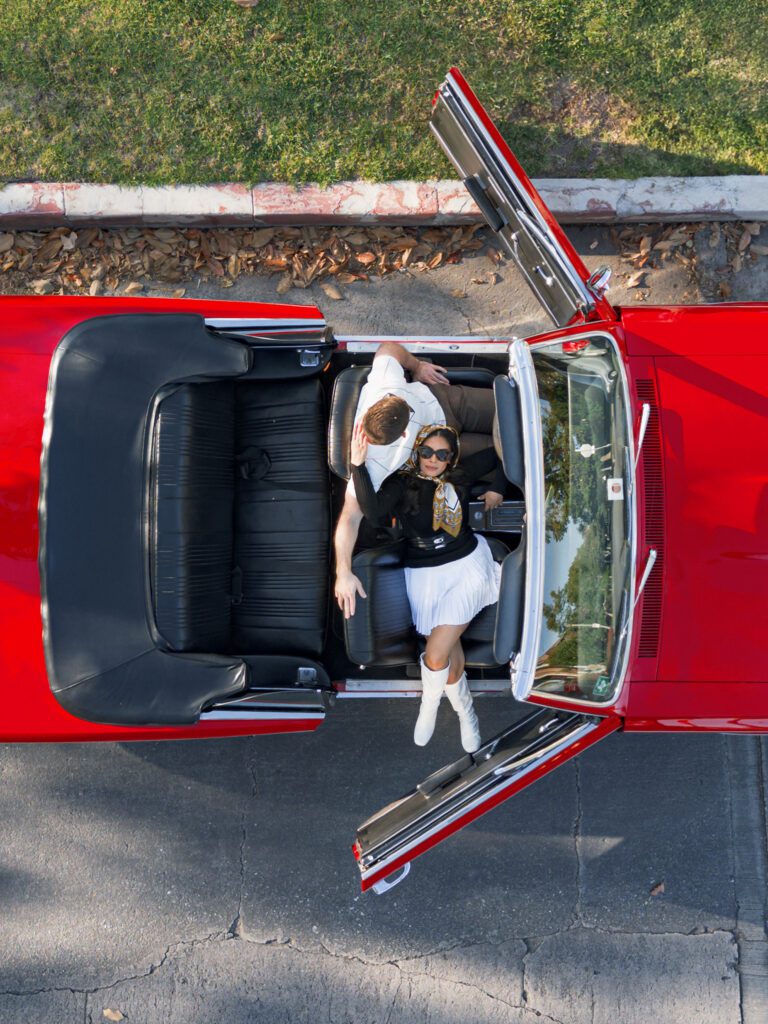 Aerial drone photo of couple lounging in a vintage red convertible