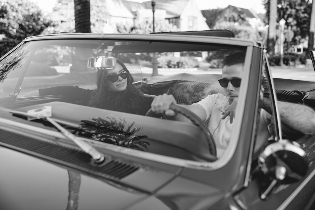 smoking man driving a convertible with his fiancé in the passenger seat