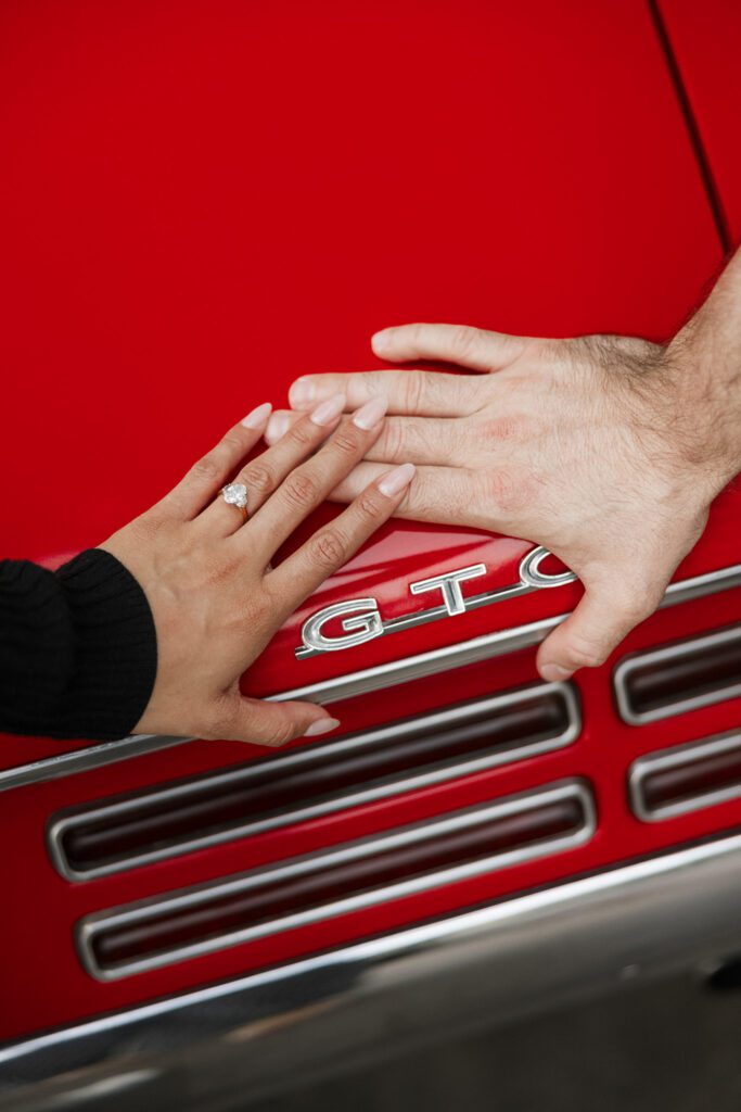 couples hands next to GTO plate on red convertible