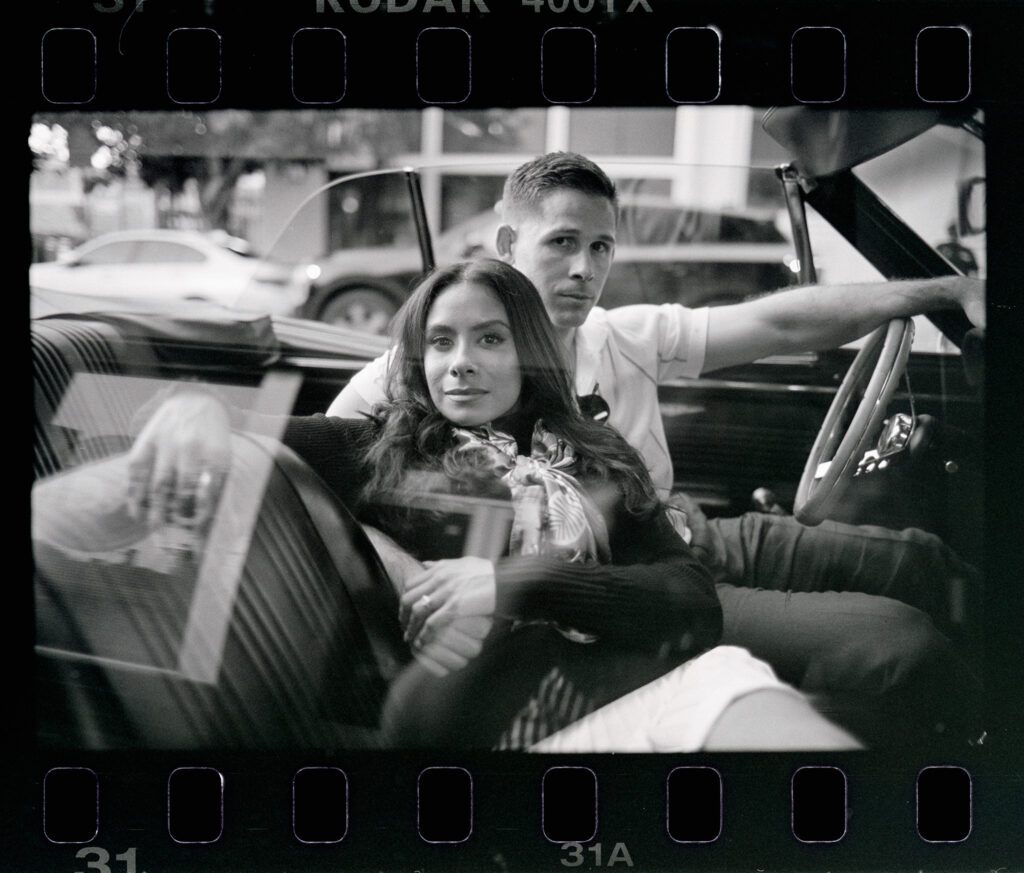couple lounging in a convertible and looking straight to camera with straight faces