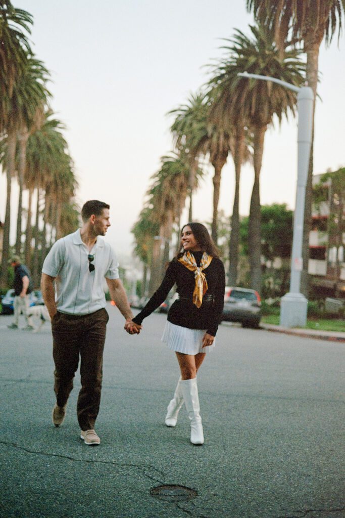 couple walking hand in hand down a palm tree lined street